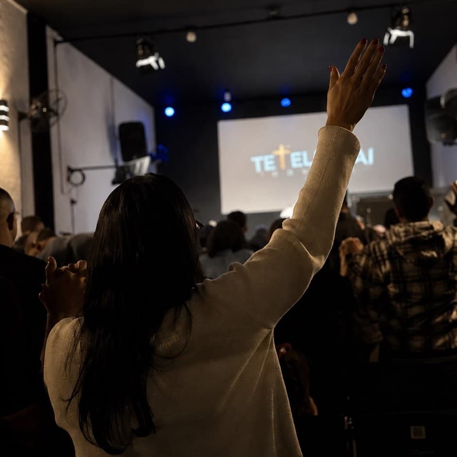 Mulher em adoração com a mão erguida durante o culto, diante do telão da igreja